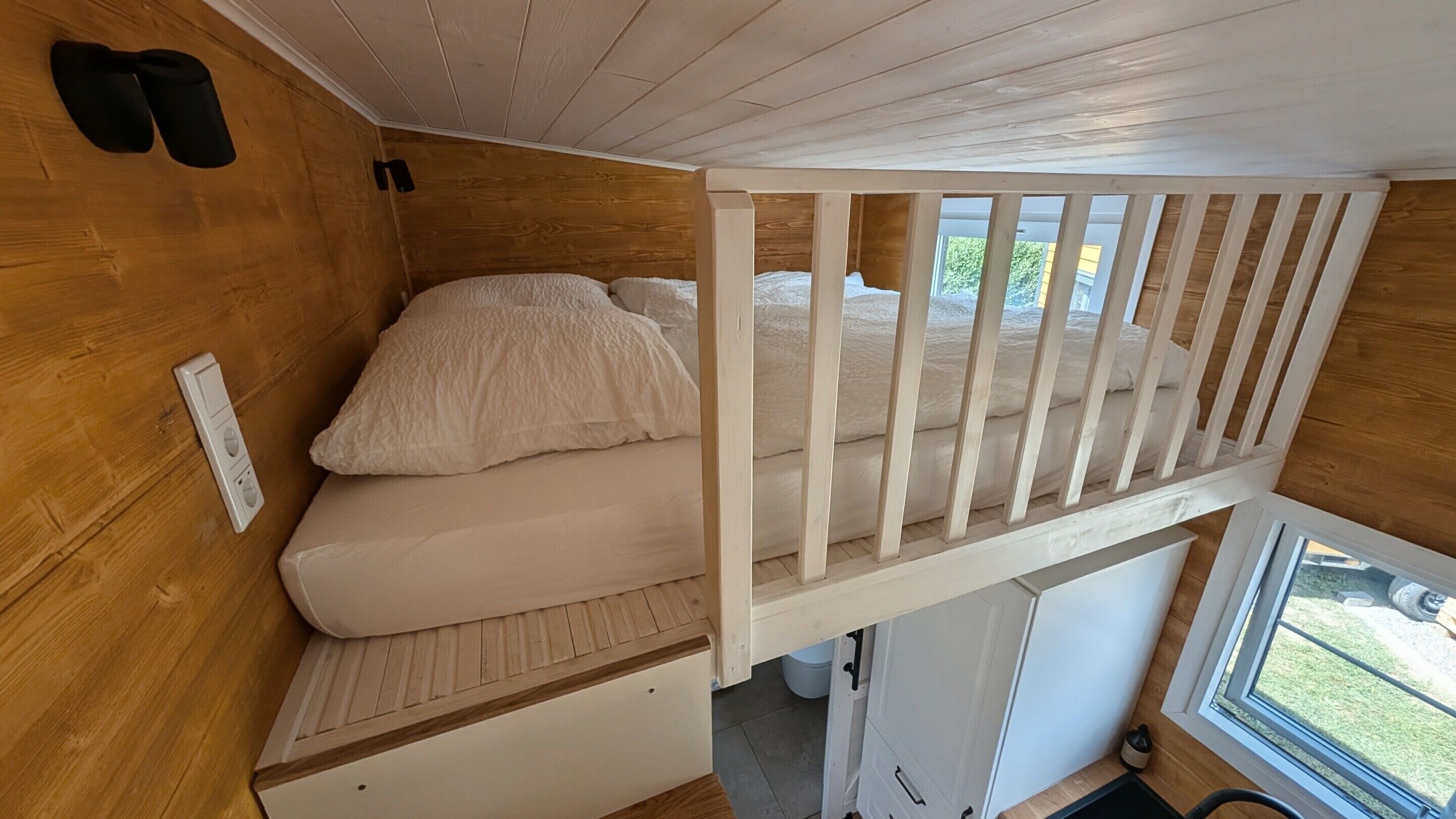 A compact bedroom with a bunk bed, wooden walls, a small window, and a white door.