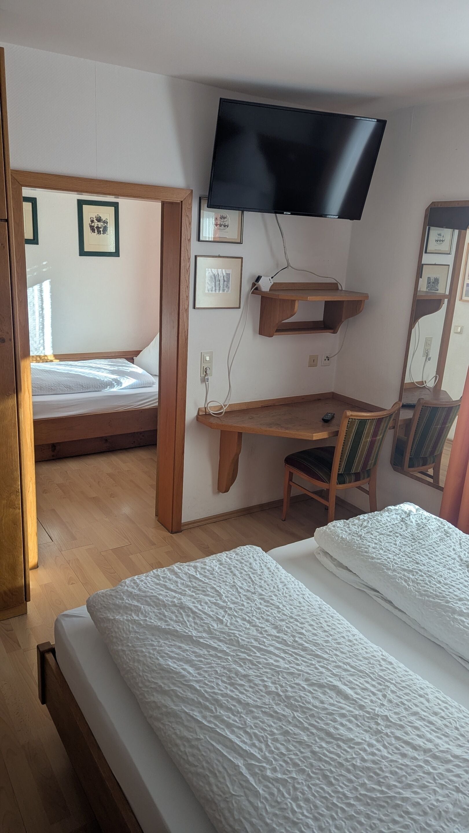 Un dormitorio con cama, escritorio, silla, televisor y cuadros en la pared.