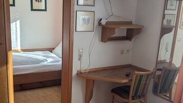 Un dormitorio con cama, escritorio, silla, televisor y cuadros en la pared.