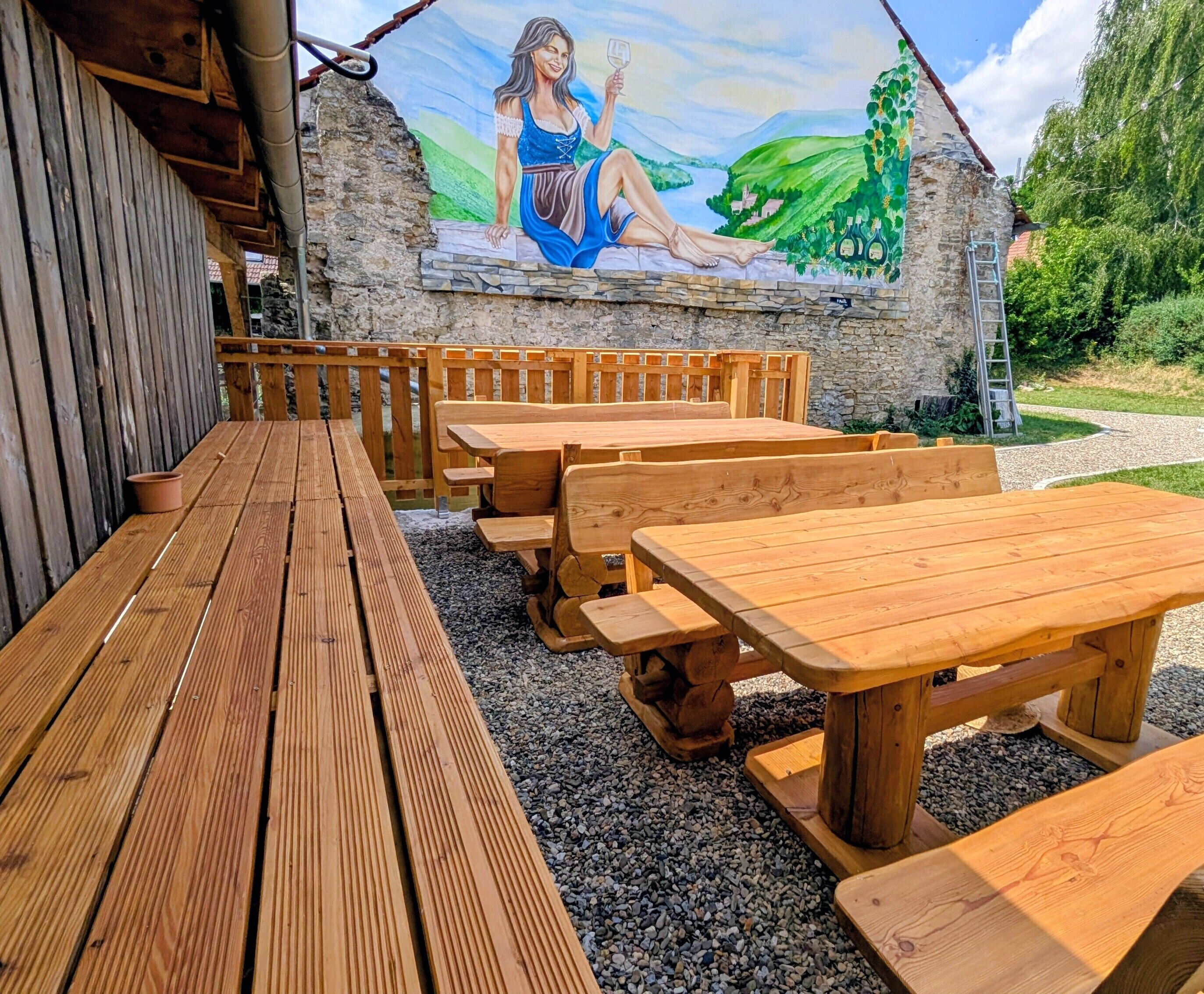 Un espacio al aire libre con bancos y mesas de madera, un mural en la pared y un camino de grava.