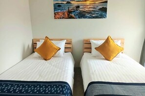 Two single beds with wooden headboards, white bedding, and a large landscape painting above. - Hug Udon (Udon Thani)
