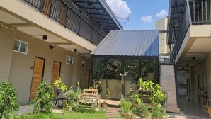 A courtyard with a glass enclosure, wooden furniture, and potted plants. - Hug Udon (Udon Thani)