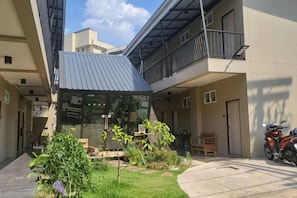 A courtyard with a covered seating area, a motorcycle, and a small garden. - Hug Udon (Udon Thani)