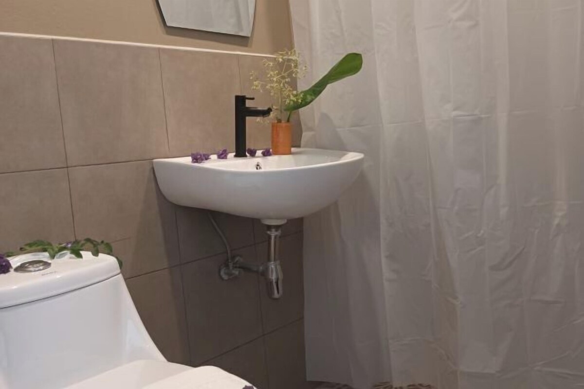 Ein Badezimmer mit einem weißen Waschbecken, einem schwarzen Wasserhahn und einer Pflanze im kleinen orangefarbenen Topf.