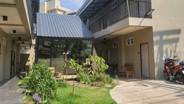 A courtyard with a covered seating area, a motorcycle, and a building with a balcony. - Hug Udon (Udon Thani)