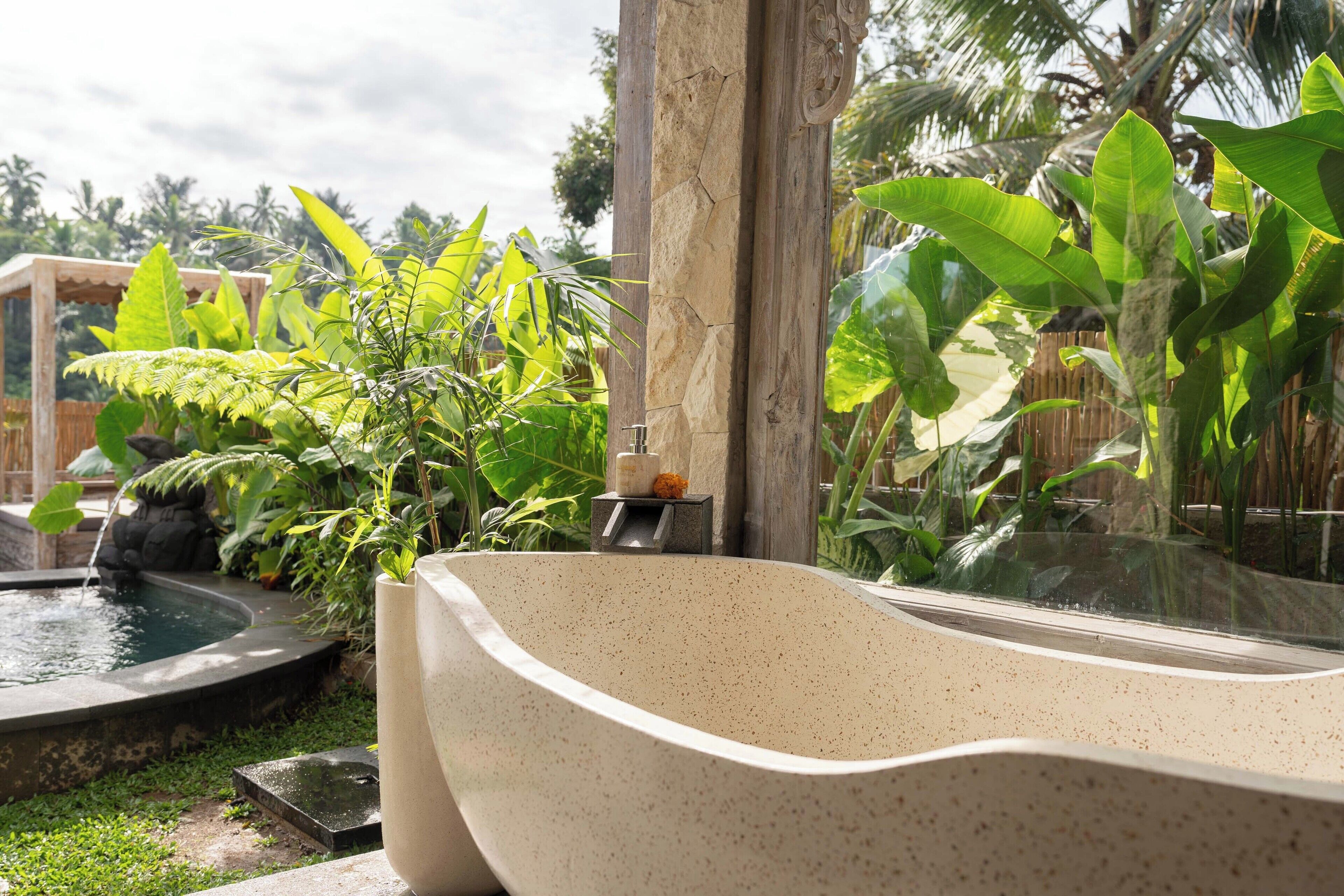 A spa area with a large freestanding bathtub, a small fountain, and lush tropical plants.