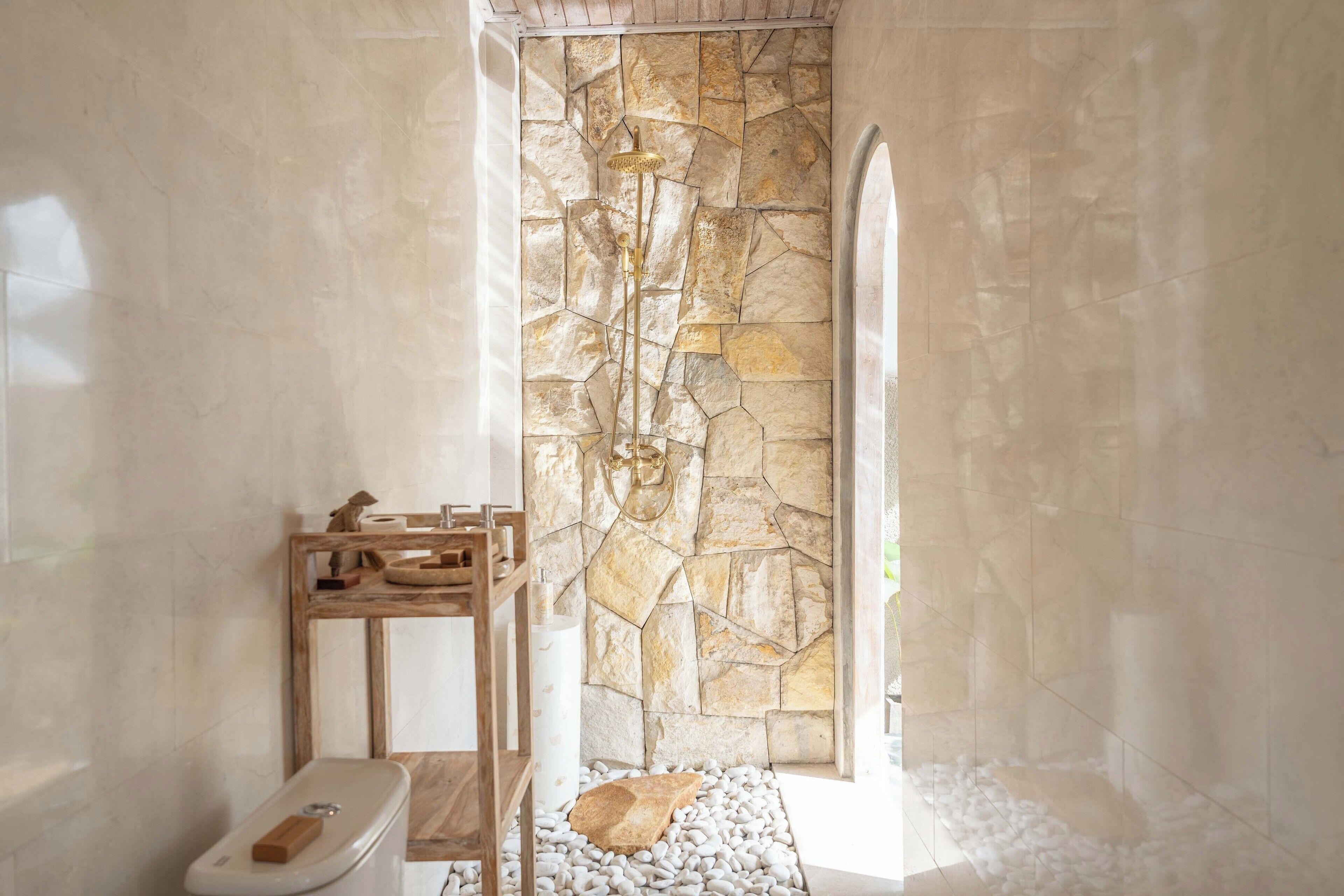 A bathroom with a stone wall, a wooden bench, a toilet, and a shower area.