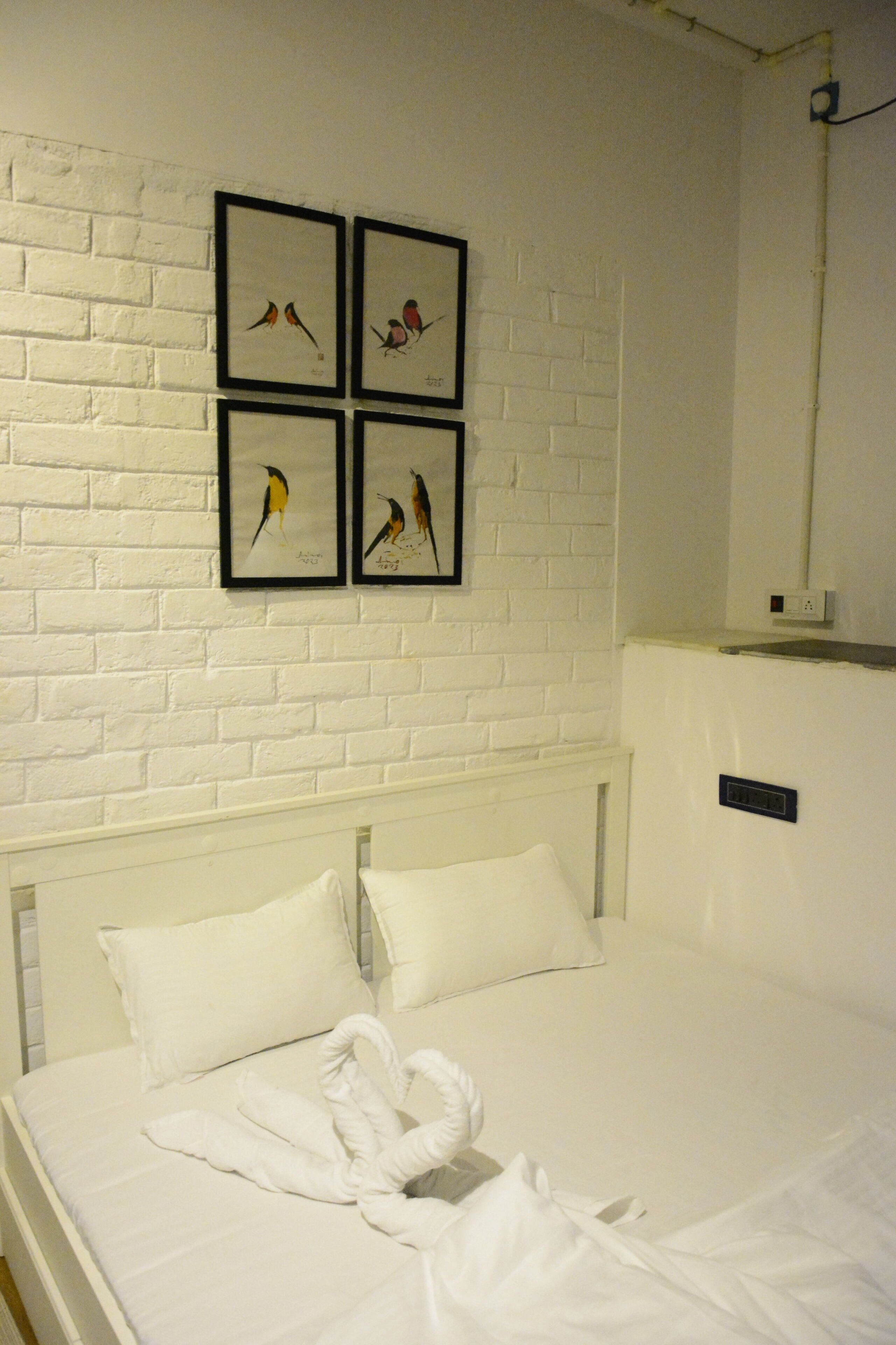Una cama bien hecha con sábanas blancas y una toalla ordenada encima. Cuatro cuadros enmarcados con pájaros decoran la pared sobre la cama.