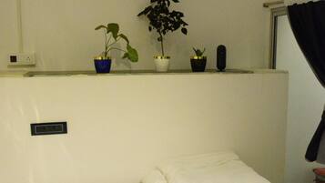 Habitación de hotel con cama, aire acondicionado de pared y tres plantas en macetas sobre la cama.