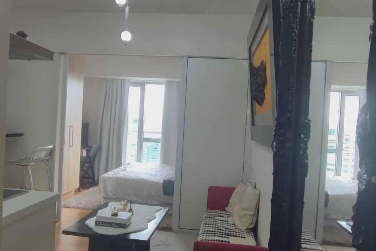 Una habitación de hotel pequeña con una cama, una mesita con un libro, un sofá rojo y una ventana.