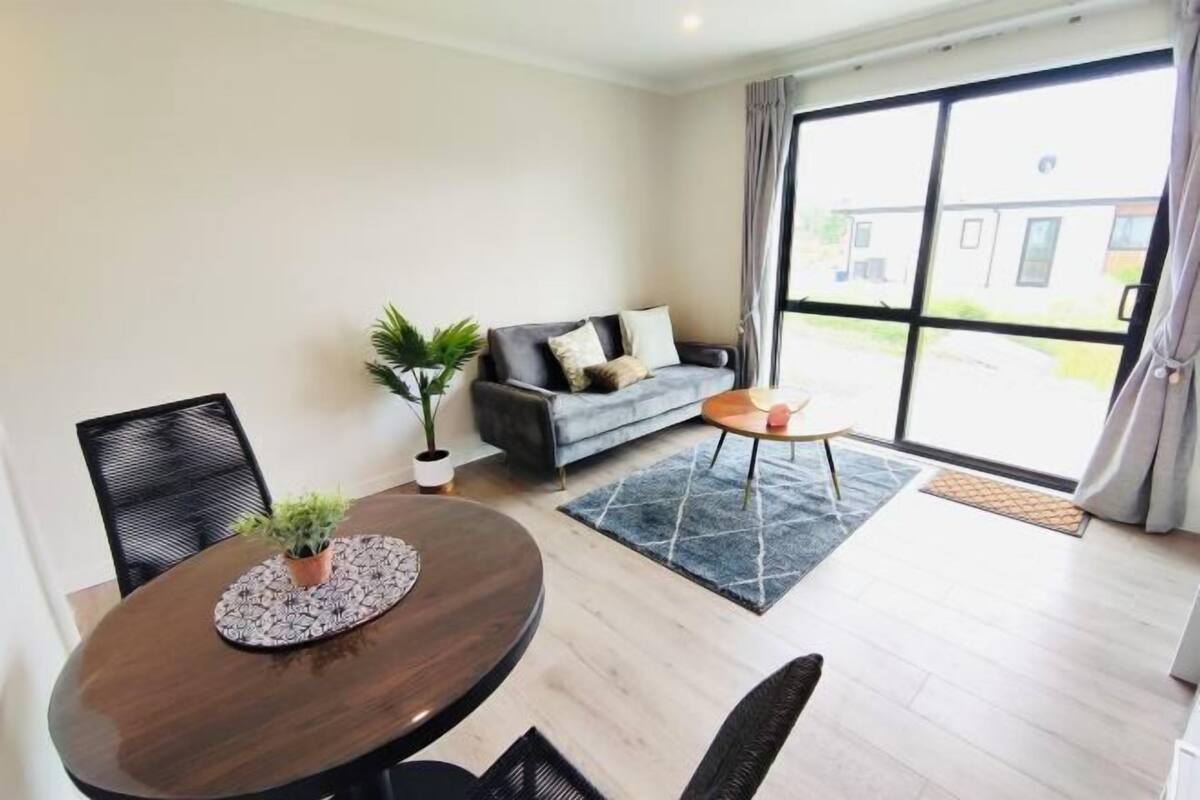 A modern living room with a round dining table, a sofa, and a large window.