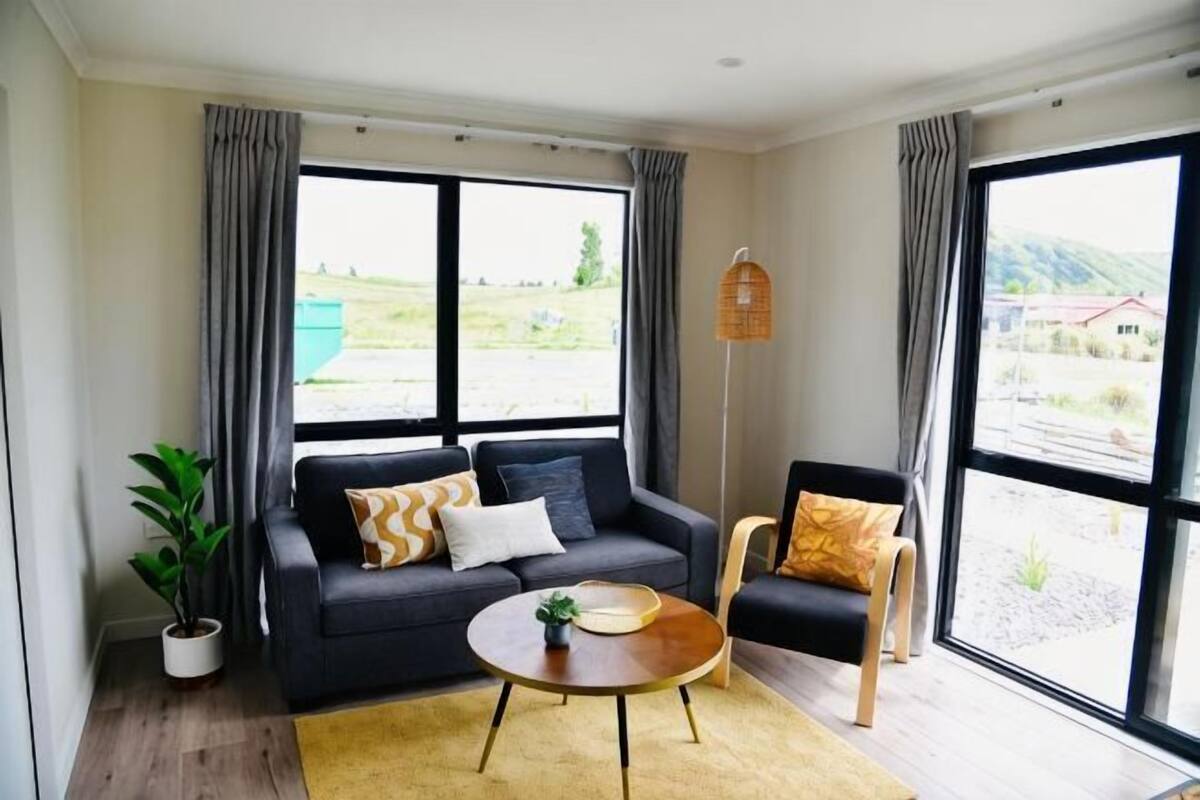 A room with a sofa, a chair, a coffee table, a floor lamp, and large windows with curtains.