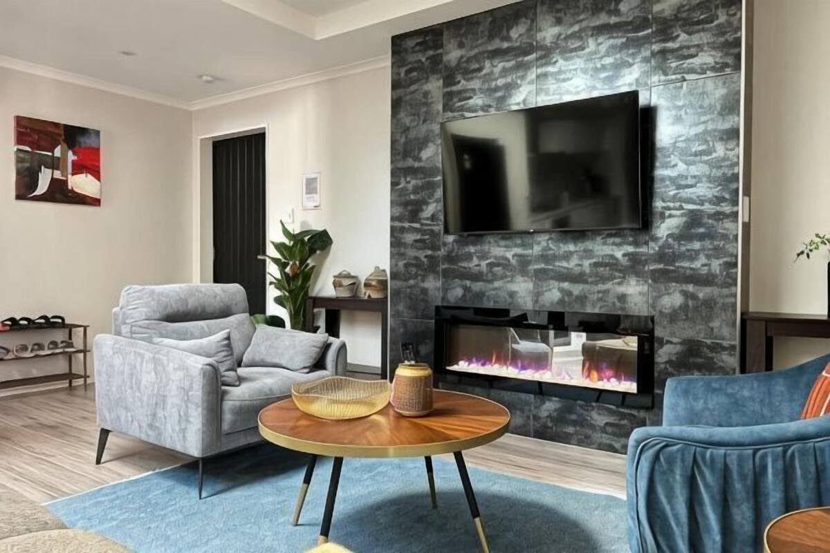 A modern living room with a fireplace, a flat-screen TV, a grey armchair, and a blue sofa.