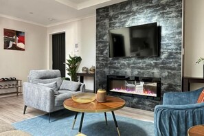 Una sala de estar moderna con chimenea, un televisor de pantalla plana, un sillón gris y un sofá azul.