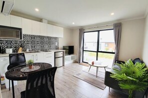 Una cocina moderna con armarios blancos, salpicadero blanco y negro, y un comedor con mesa y sillas redondas.