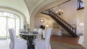 Een eetgedeelte met een ronde tafel, witte stoelen en een trap naar een hoger niveau.