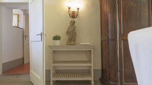 Een gang met een witte deur, een tafeltje met een beeldje en een wandlamp.