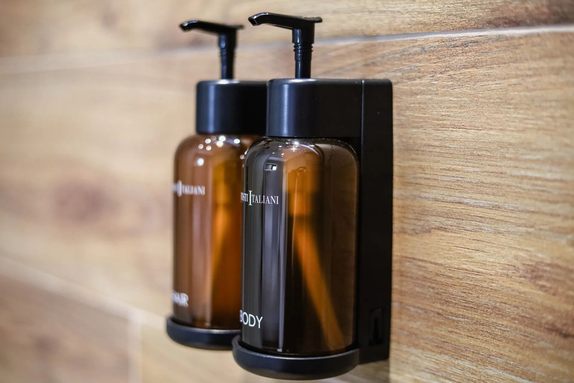 Two body care dispensers mounted on a wooden wall.