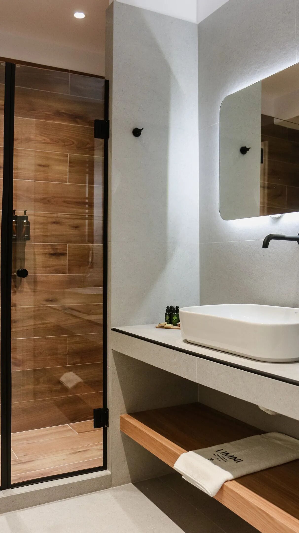 Een moderne badkamer met een douchecabine van glas, een witte wastafel en een spiegel erboven.