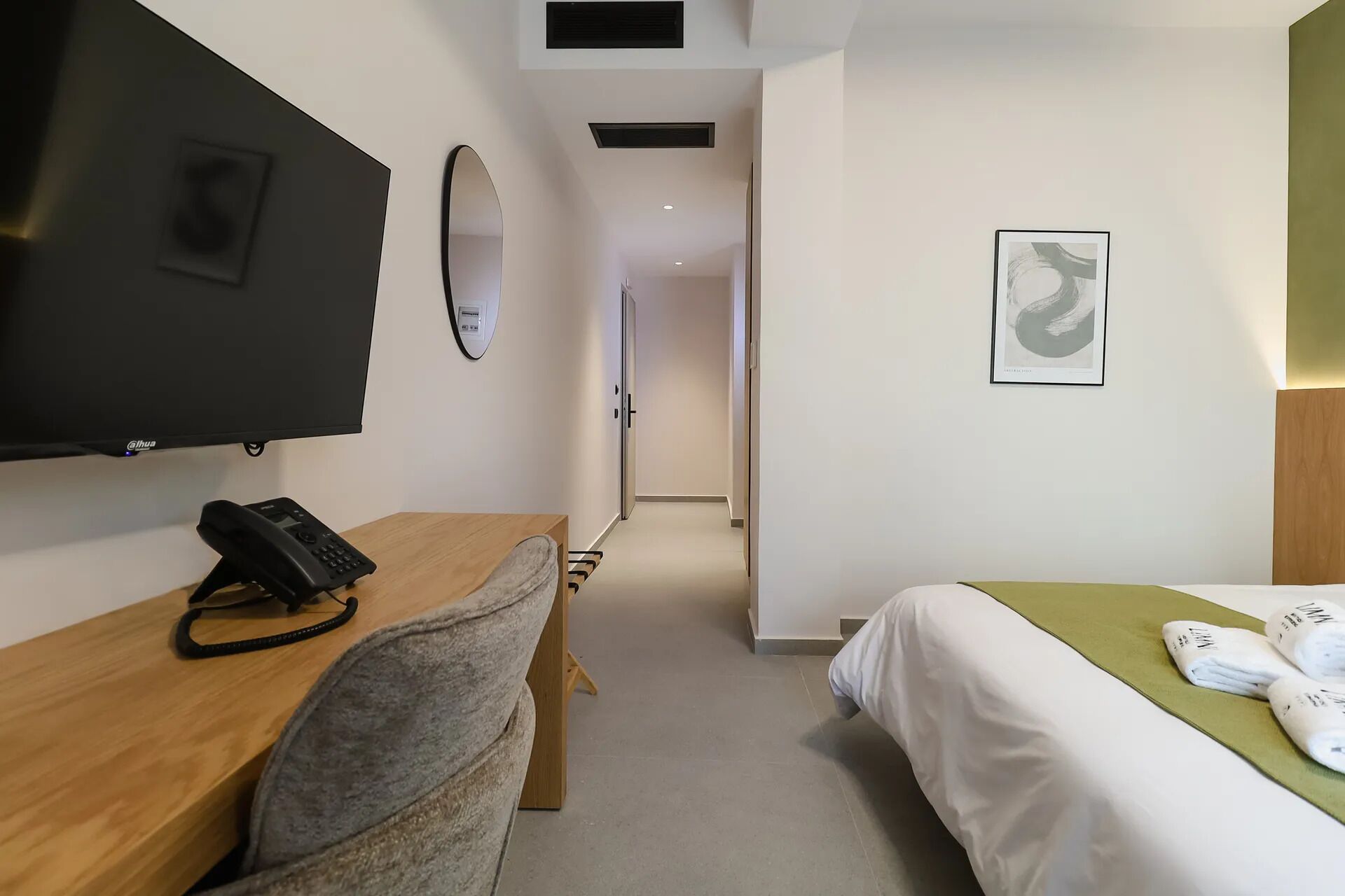 A hotel room with a bed, a desk with a telephone, a television, and a door leading to another room.