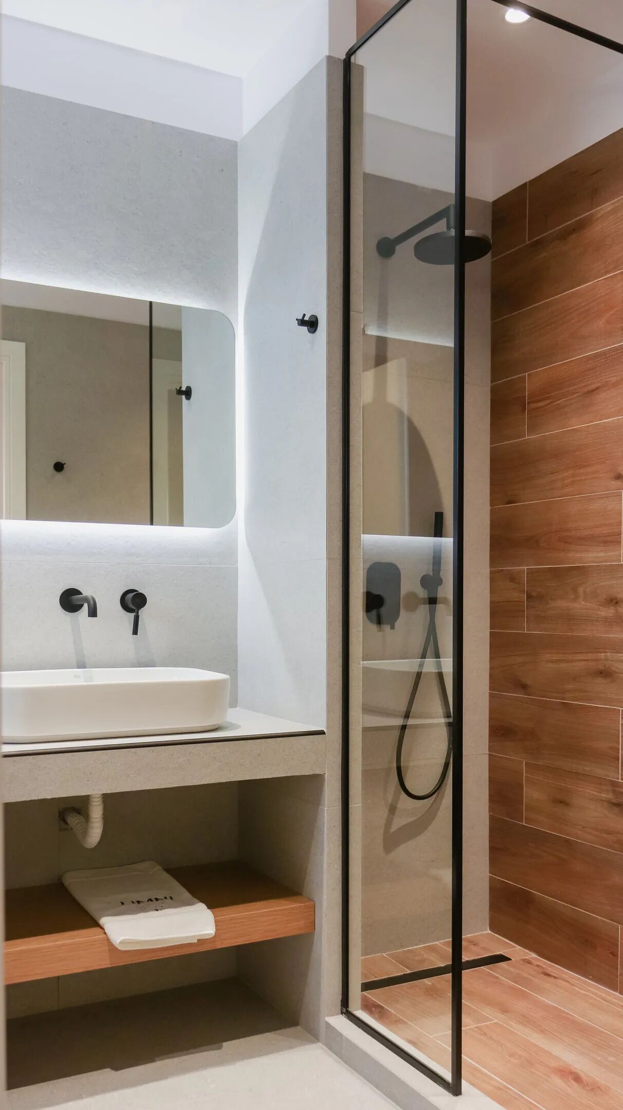 A modern bathroom with a glass-enclosed shower, a white sink, and a wooden vanity.