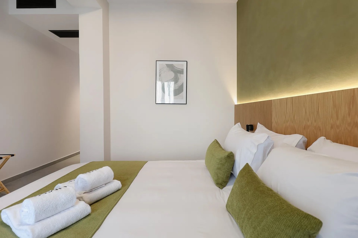 A hotel room with a bed, green towels, a framed picture on the wall, and a wooden headboard.
