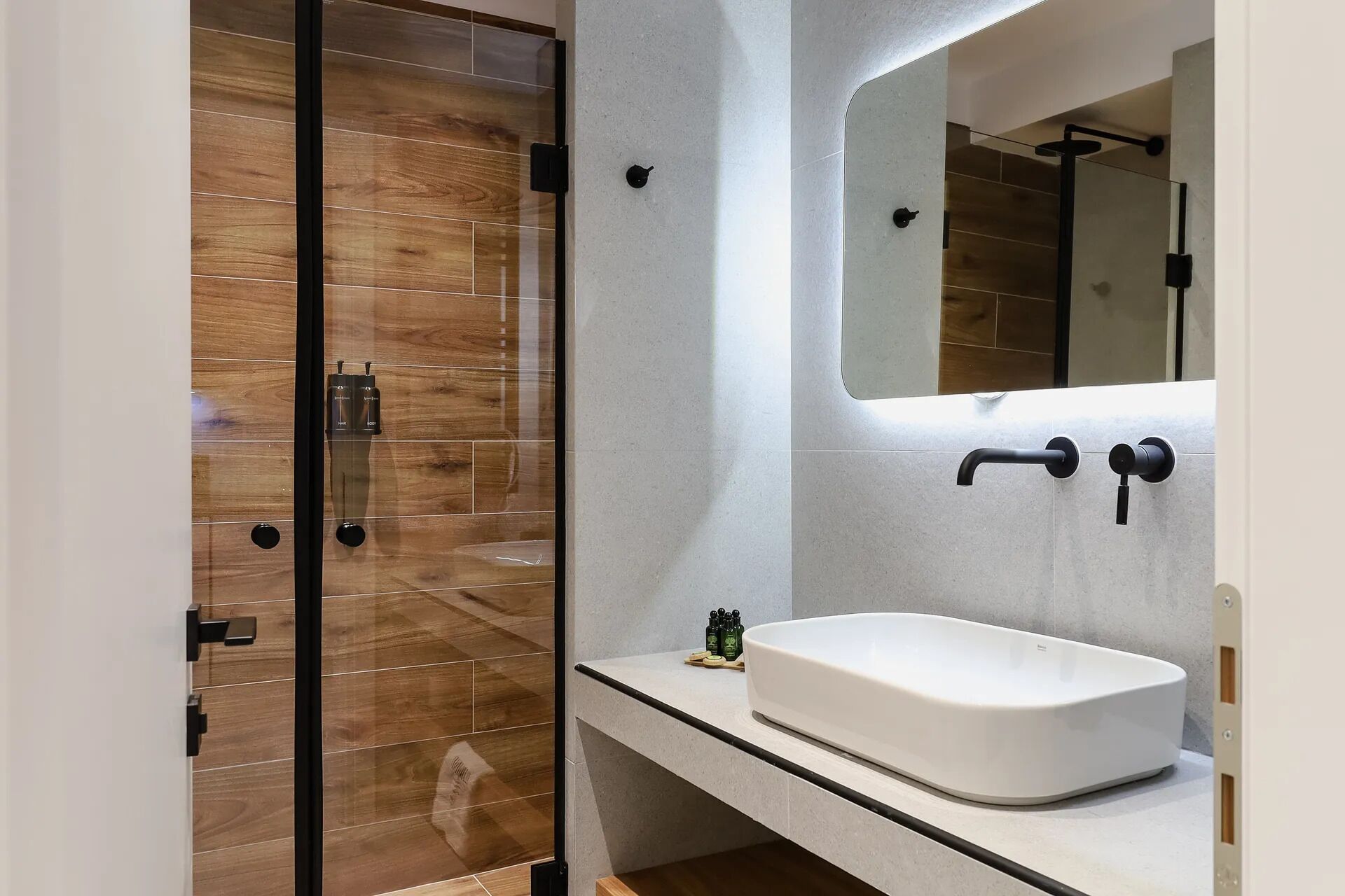 A modern bathroom with a wooden shower enclosure, a white sink, and a large mirror.