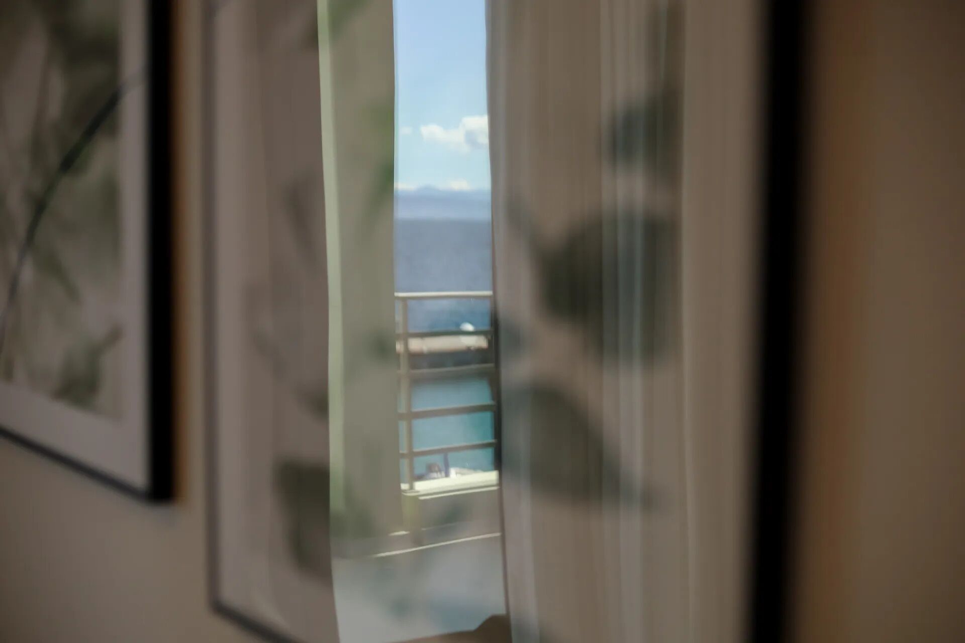 Blick durch ein Fenster mit Metallgitter, der zu einem Balkon mit freiem Meerblick führt.