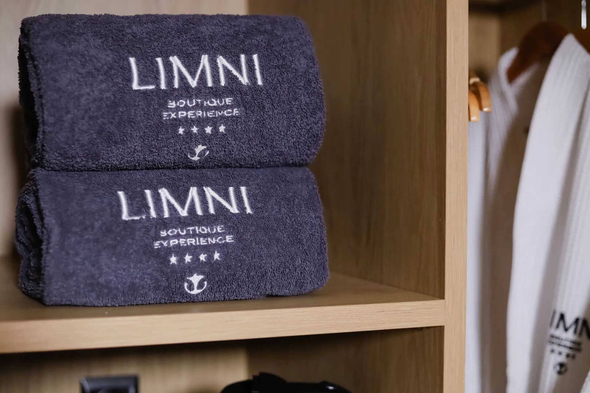 Two folded towels with 'LIMNI' and 'BOUTIQUE EXPERIENCE' printed on them, placed on a wooden shelf.