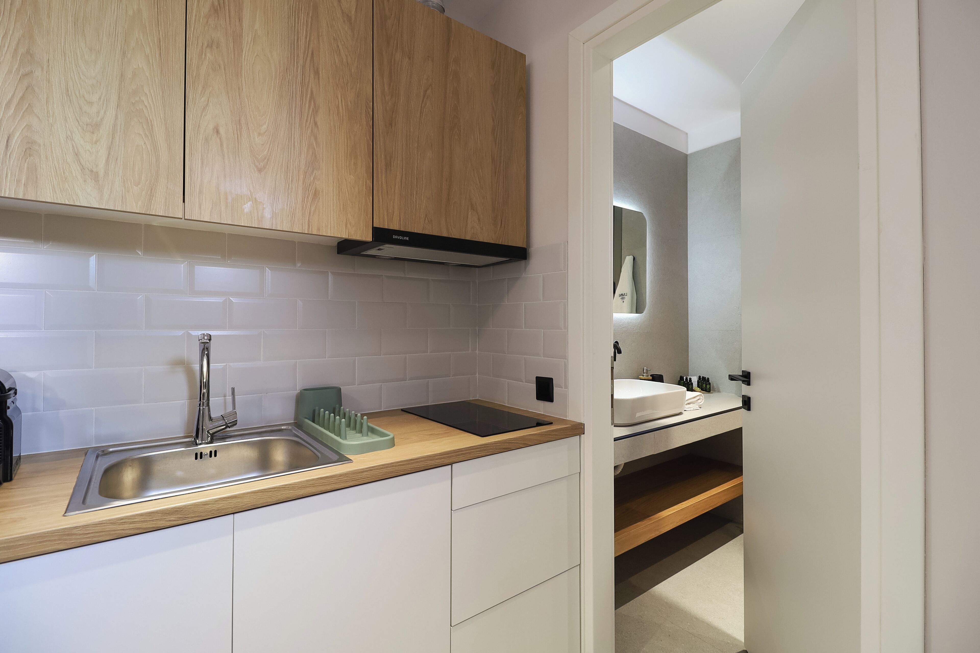 Una cocina moderna con un lavamanos de acero inoxidable, armarios de madera y un salpicadero de azulejos blancos.