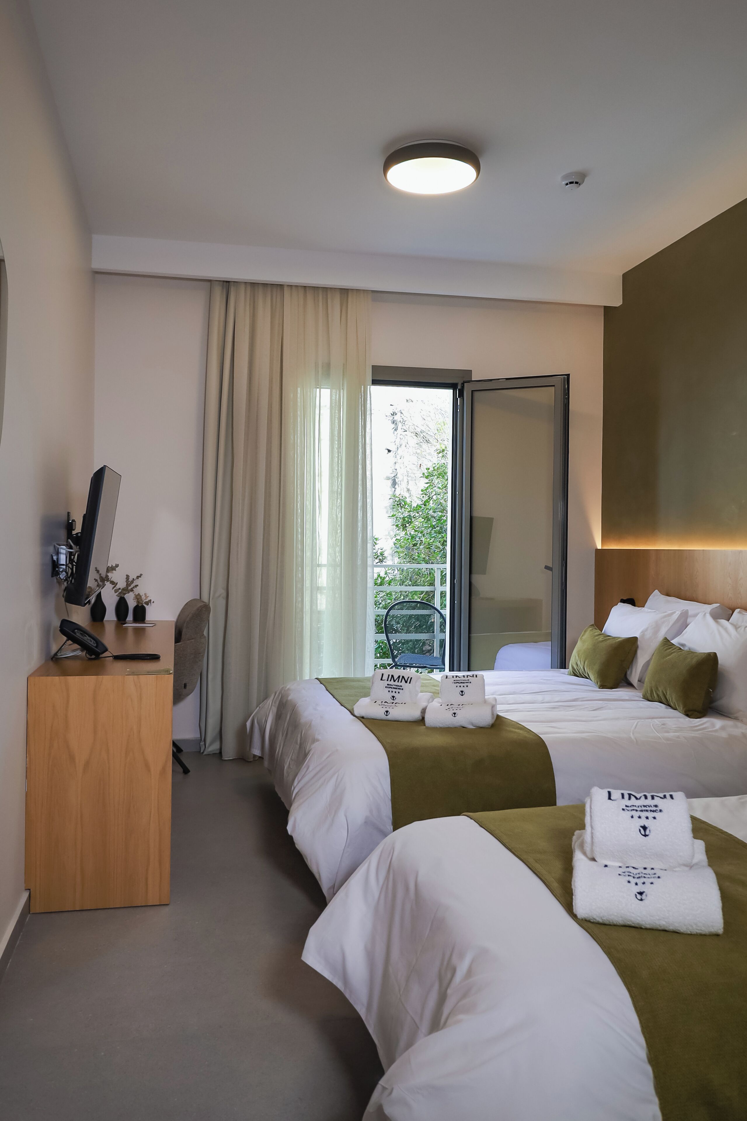 Camera d'albergo con due letti, una scrivania, una sedia, un computer e vista sul verde.