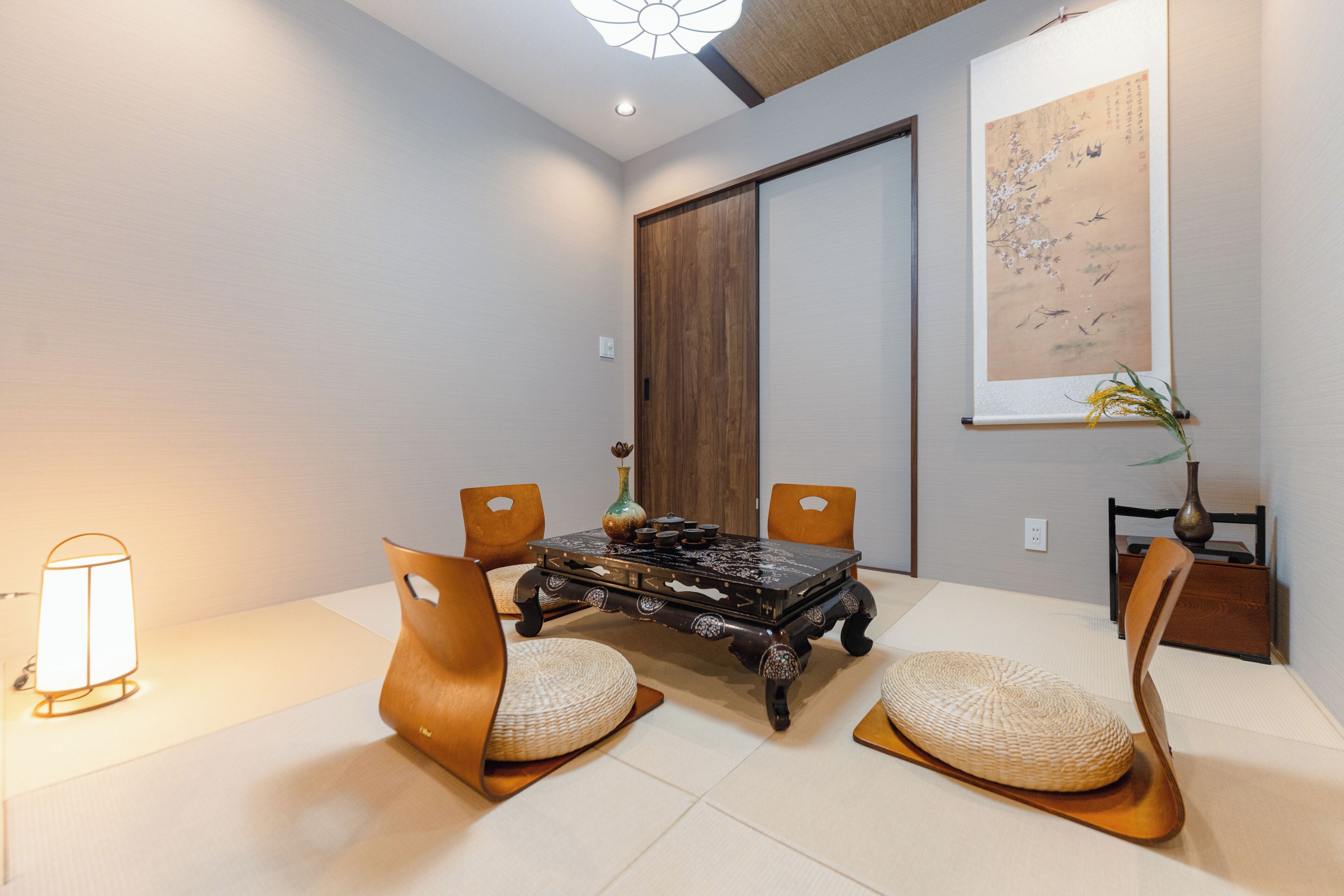 A traditional Japanese-style room with tatami flooring, a low table with a dark wooden top, and two wooden chairs with woven cushions.