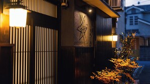 A building facade with vertical slats, a security camera, and a wall-mounted light fixture. - Kyoto Amazing - The Wizard of Oz (Kyoto)