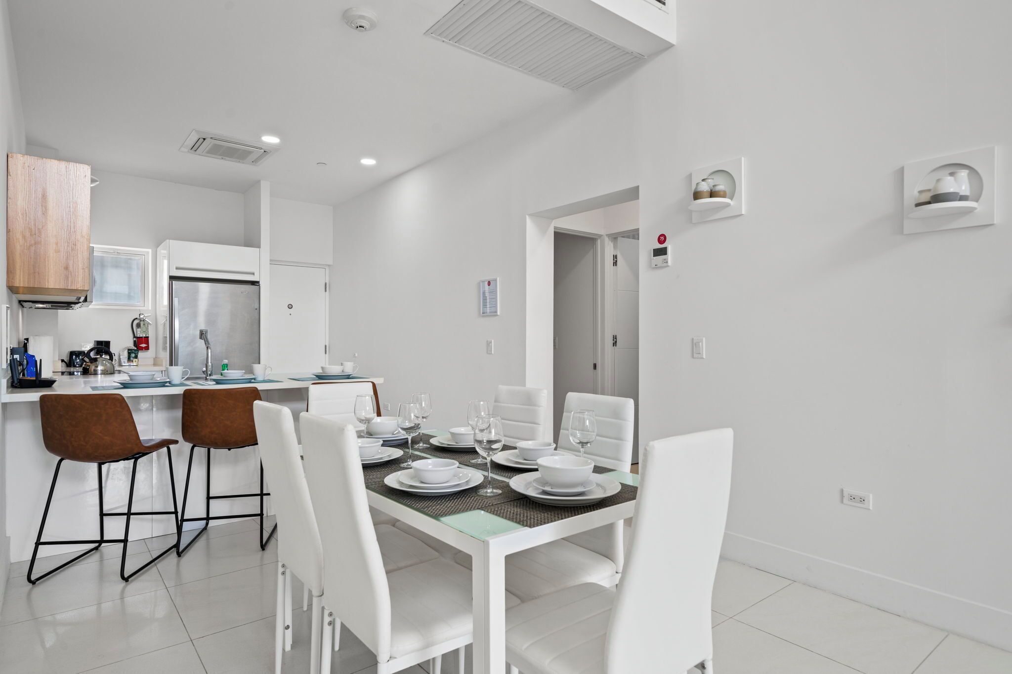 A modern kitchen with white cabinetry, a stainless steel refrigerator, and a dining area with white chairs and a glass table.