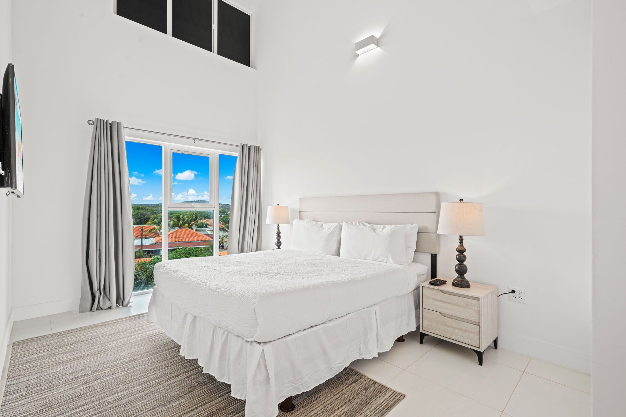 A bedroom with a large bed, a nightstand with a lamp, and a view of the outdoors through a sliding door.