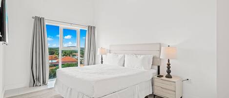 A bedroom with a large bed, a nightstand with a lamp, and a view of the outdoors through a sliding door.