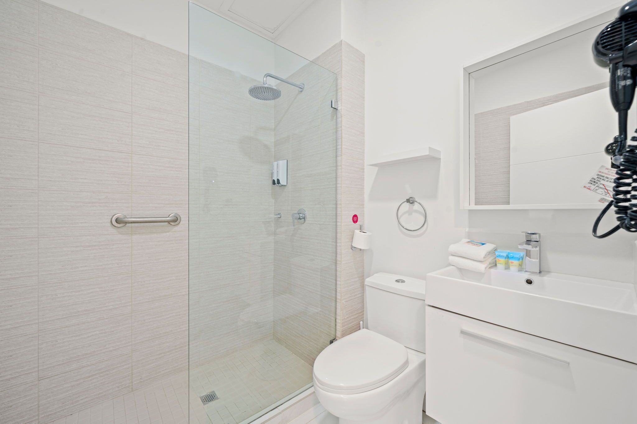A modern bathroom with a glass shower enclosure, a white toilet, and a sink with a hairdryer on the countertop.