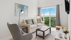 A modern living room with a sofa, armchair, coffee table, and a view of greenery through large windows. - Aruba's Life 306 (Noord)