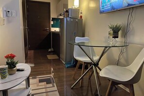 Un espacio habitable compacto con kitchenette, un comedor con dos sillas, una mesita y un televisor montado en la pared.