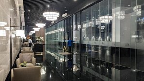 Un hall d’hôtel moderne avec un mur en verre réfléchissant, un espace salon avec des fauteuils et une personne qui nettoie le sol.