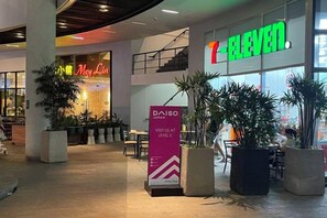 Una tienda 7-Eleven con un letrero, plantas en macetas y un anuncio de DAISO en un centro comercial.