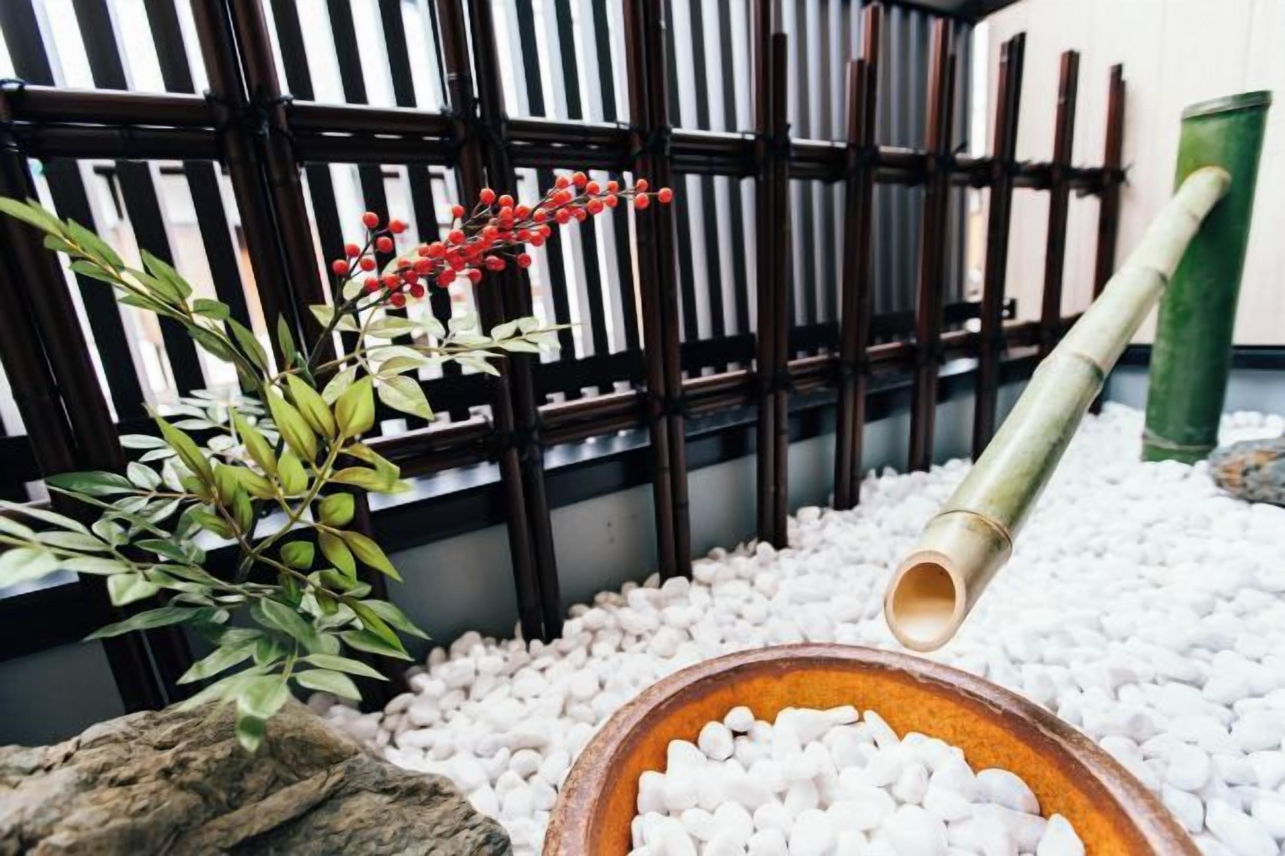 A traditional Japanese garden with a bamboo water feature, white pebbles, and a wooden bowl.