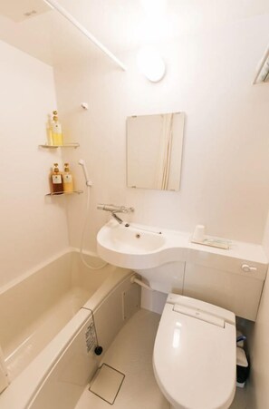 Un baño con bañera, lavabo e inodoro. Hay repisas con artículos de aseo y un espejo sobre el lavabo.