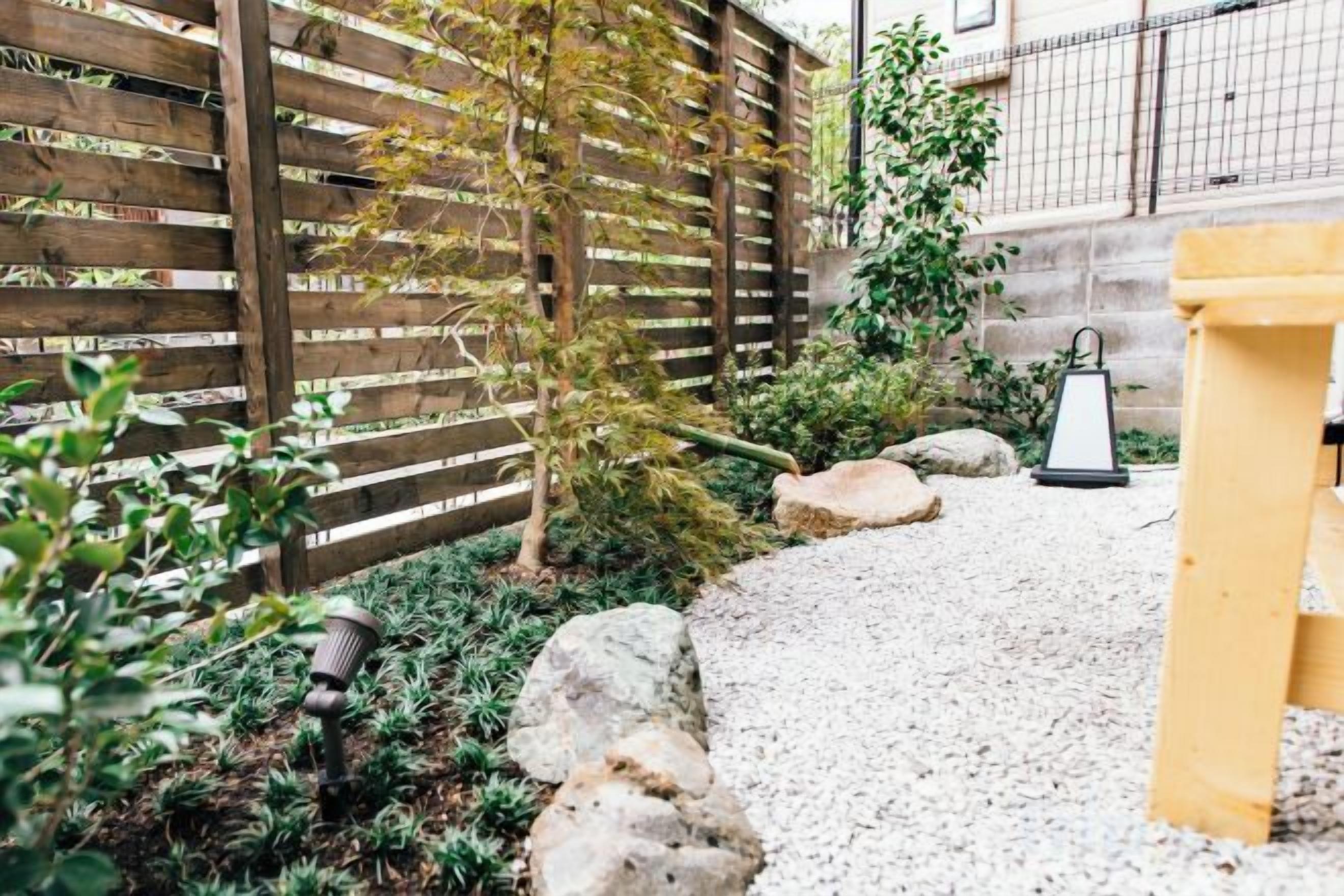 A garden with a wooden fence, a gravel path, and a lantern.