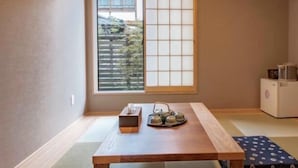 Una habitación japonesa tradicional con suelo de tatami, una mesa de madera baja, una ventana con pantalla shoji y un pequeño equipo de aire acondicionado.