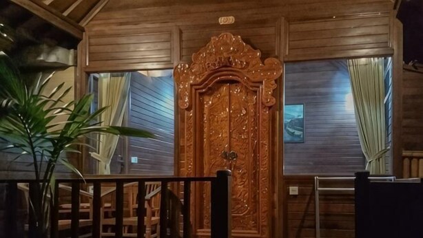 A wooden door with intricate carvings, a dining area with chairs, and a potted plant.