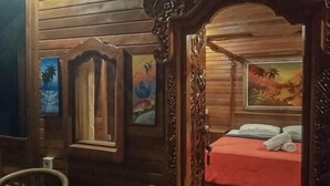 A wooden room with a bed, a chair, and paintings on the walls.