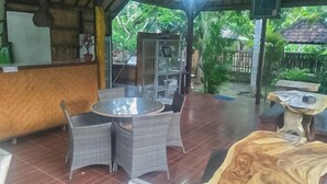 A covered outdoor seating area with wicker chairs and a round table, a wooden sculpture, and a bar area with a counter and stools.