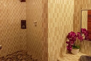 Une salle de bain avec un mur carrelé, une douche, un lavabo et une orchidée en pot.