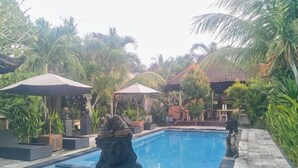 A swimming pool with a statue, surrounded by palm trees and covered seating areas.